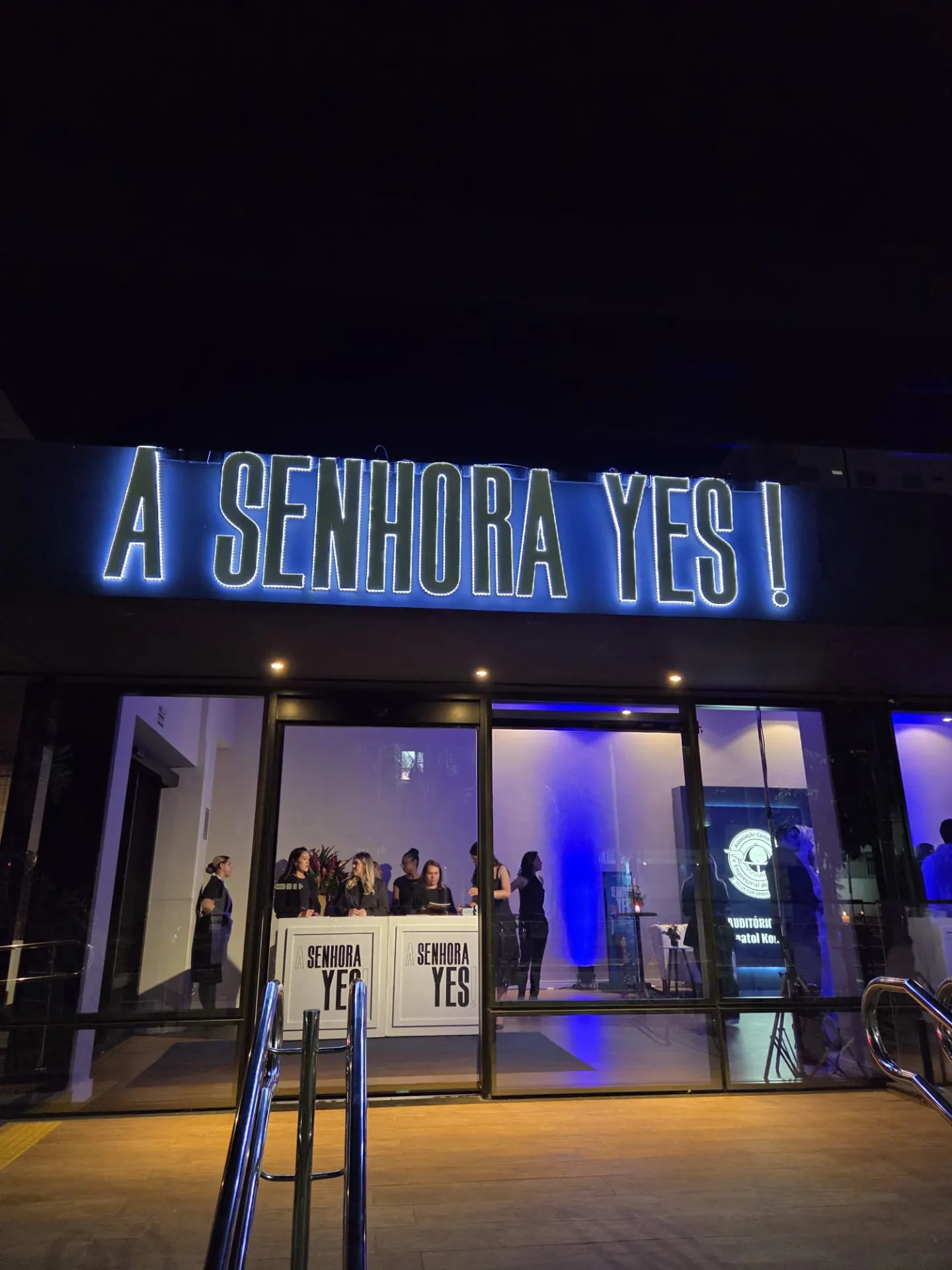 Fachada iluminada com o letreiro A Senhora Yes! no evento de lançamento